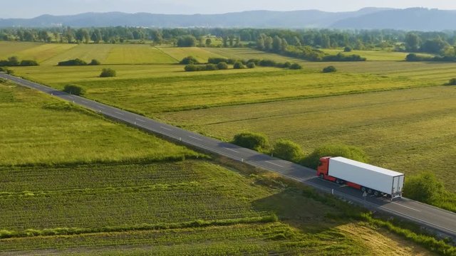 Aerial shot of a fast truck on the road in beautiful countryside with green grass in the summer.
