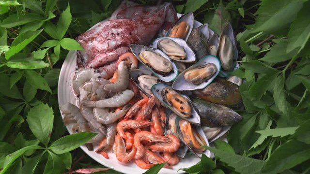 Raw mussles squid and prawns are on the board in the greens outdoors, meals with fish, seafood dish, roasted and grilled fish, preparations for barbecue, grill and fire, asian cuisine meals