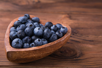 Wooden bowl in the shape of heart with blueberries standing on brown rustic background. Healthy food