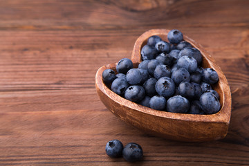 Wooden bowl in the shape of heart with blueberries standing on brown rustic background. Healthy food