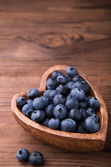 Wooden bowl in the shape of heart with blueberries standing on brown rustic background. Healthy food