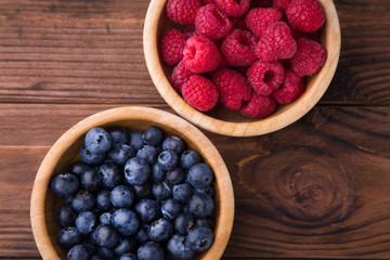 Two wooden bowls with raspberries and blueberries standing on brown wooden background. Summer fruits and berries. Healthy food
