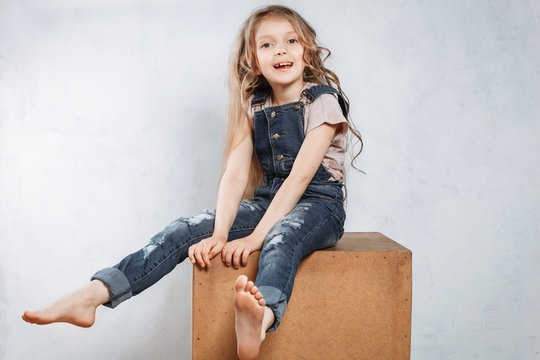 Happy and funny stylish little girl smiling in fashion jeans over grey background.