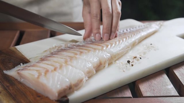 Chef is slicing raw codfish on the board before roasting it, cooking outdoors, fish grill and barbecue