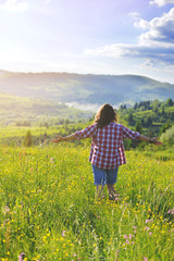 The girl raised her hands and stands on a meadow in the mountains in the summer