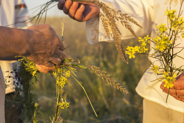 A girl and man in white traditional Slavic dress wreathes a wreath of fresh wildflowers at sunset. Russian traditions