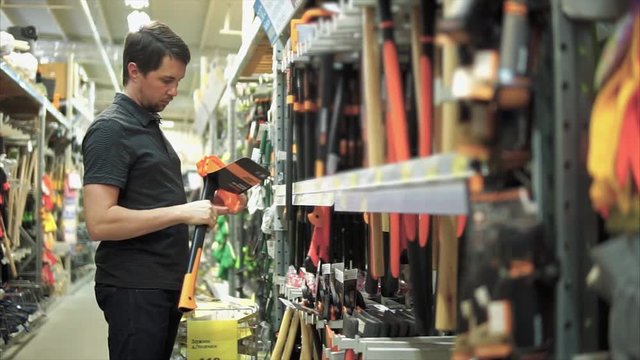 Man in the mall near shelves with tools. He taking axe and studying its quality. Purchase for camping trip