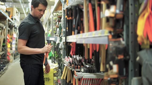 Handsome man in the store. He looking at the little axe in tool store. Customer buying axe for the work