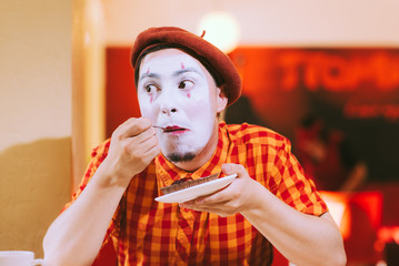 The clown is eating a cake in a cafe and his face is croaking.