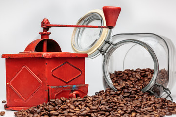 Vintage coffee grinder beside overturned glass jar with coffee beans, on white background