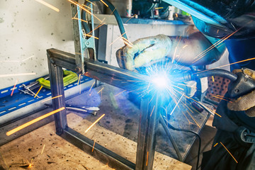 Close up A strong man is a welder in a black T-shirt, in a welding mask and gloves, a metal product...