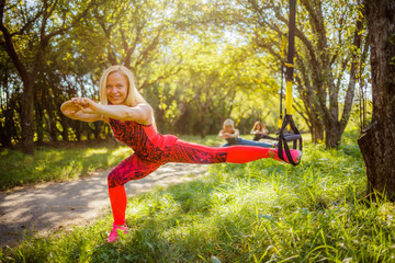 Three beautiful healthy fitness blonde performs exercises for the hips on a sports suspension...
