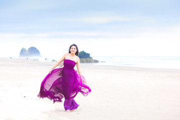 Fototapeta na wymiar Young woman in flowing magenta dress standing on beach