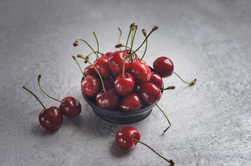 Fototapeta na wymiar Vase with ripe red cherries on a gray wooden background. .