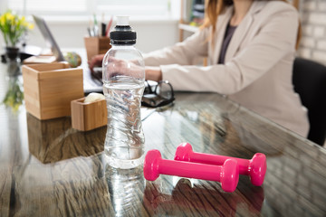 Water Bottle And Fitness Dumbbells On Office Desk