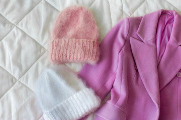 Women's draped pink coat next to two fluffy caps of different colors