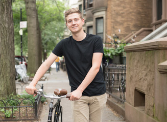 Portrait of young modern hipster man pushing bicycle on a residential street in the city