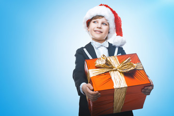 Beautiful little boy with a big Christmas gift in a Santa Claus hat. Christmas gifts for children. Smart boy Celebrates Christmas. New Year's holidays
