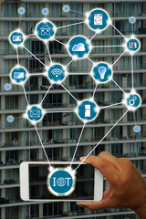 Internet of things (IOT) concept : Hand holding smartphone controlling various household equipment with building background. Smart home concept, Smart Building Concept.