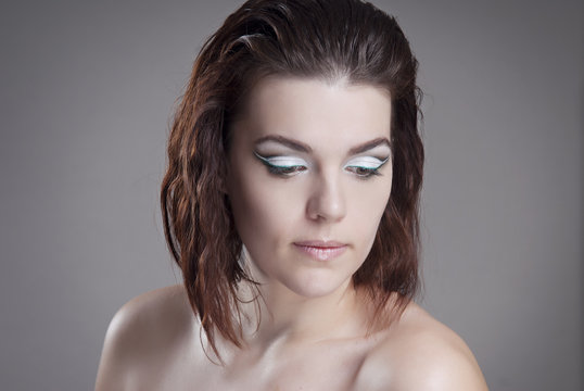 The girl the brown-haired woman with bright makeup looking down. Isolated grey background. Hairstyle graduated bob.