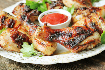 Grilled chicken legs on wooden table served on white plate with coriander
