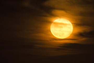 a warm orange full moon rises into a cloudy night sky