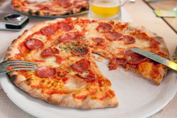 Sausage pizza on a white plate with fork and knife. Cut.