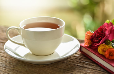 White cup of hot tea by the garden with roses and notebook background. Selective focus, soft light effect added.