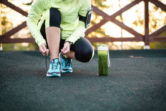 Green detox smoothie cup and woman lacing running shoes before workout.
