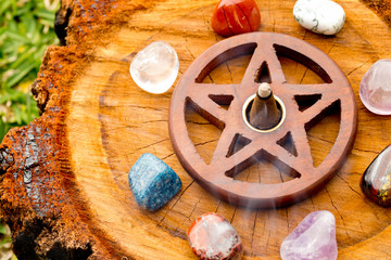 Burning incense cone  in wooden pentacle incense holder on natural cut tree log with variety of...