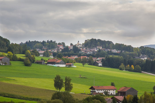View towards a small town in the bavarian forest with a grey cloudy sky, green fields and trees