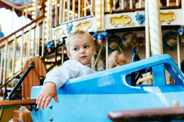 Fototapeta na wymiar Happy little boy ride in a vintage blue airplane on a merry-go-round
