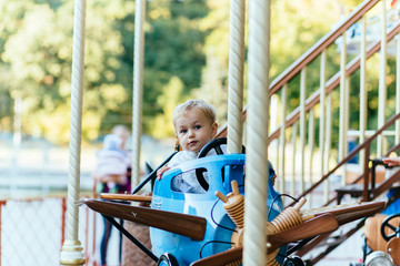 Obraz premium Happy little boy sitting in a vintage blue airplane on the merry-go-round
