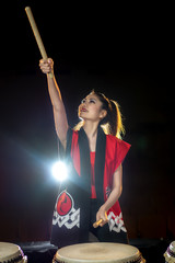 beautiful asian taiko drummer girl in red with drumsticks, studio shot on a dark background.