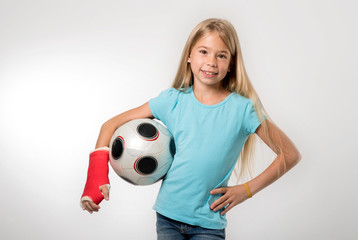 junges Mädchen mit gebrochenem Arm hält Fußball und lächelt in die Kamera