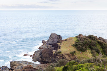 Two people explore a distant coastline trail on a beautiful grassy headland by the Pacific Ocean near Port Macquarie, Australia.