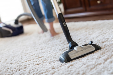 Woman using a vacuum cleaner while cleaning carpet in the house. - obrazy, fototapety, plakaty