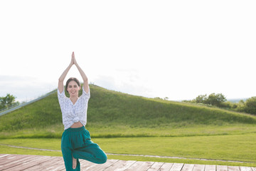 Fototapeta na wymiar Woman doing yoga outdoor. Young woman exercising vital and meditation for fitness lifestyle at the nature background in green park on wooden platform. Concept Yoga freedom