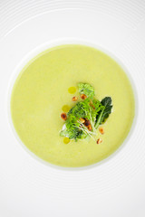Cream of broccoli soup, served with pine nuts close-up in a white plate..