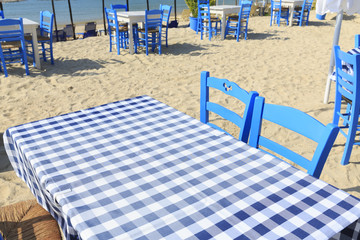 Picnic table with white and blue table cloth by the sea in Greece, Empty picnic table for product display, Defocused beach in the background