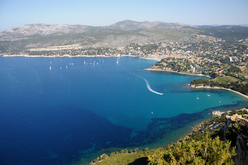 A sea bay, a view from a cliff. Sailboats and boats swim in the sea. Town is near the sea.