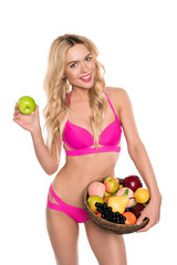 beautiful blonde woman in pink bikini holding apple and basket with fruits, isolated on white