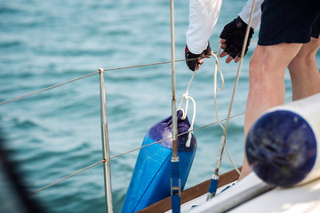 Sailor tied fenders on a yacht during the mooring to the shore. - obrazy, fototapety, plakaty