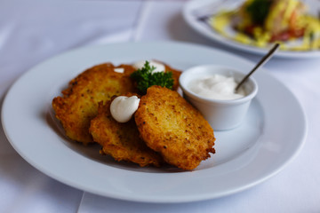 Potato pancakes - draniki - with sour cream in a white plate. The national dish of Russian, Ukrainian and Belarusian cuisine