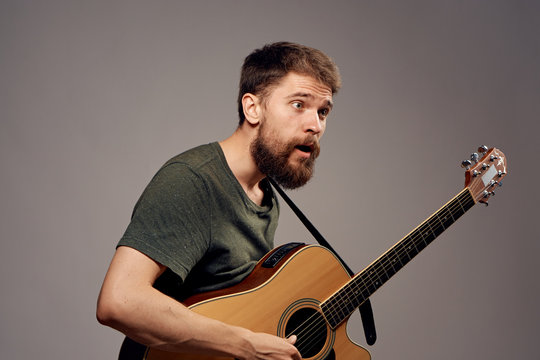 Young guy with a beard on a gray background holds a guitar