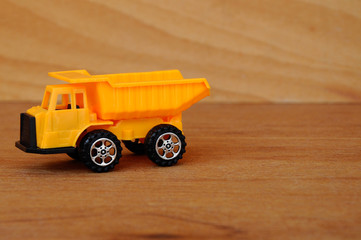 Small heavy construction machine toy, lorry. Made of plastic isolated on a wood grain texture...