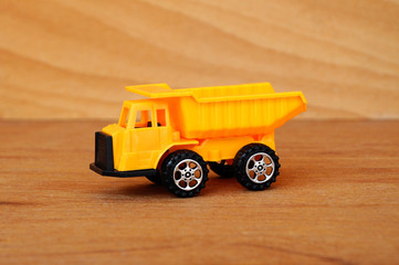 Small heavy construction machine toy, lorry. Made of plastic isolated on a wood grain texture...
