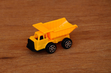 Small heavy construction machine toy, lorry. Made of plastic isolated on a wood grain texture...
