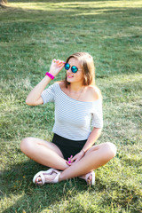 young beautiful happy woman sitting on the grass in sunglasses