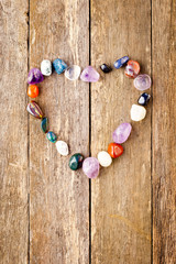 Tumbled healing crystals in heart shape on wooden background